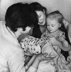 Detailed black and white graphite pencil drawing of a loving family. A father is holding a swaddled newborn baby, while the smiling mother and a young toddler girl look down at the baby affectionately.
