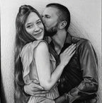 A detailed black and white graphite pencil drawing of a romantic couple embracing. A bearded man in a dark button-down shirt is gently kissing the cheek of a smiling woman. She has long hair tied half-up, is wearing a light-colored dress with ruffled sleeves, and rests her hand on his chest while his arms wrap around her waist.