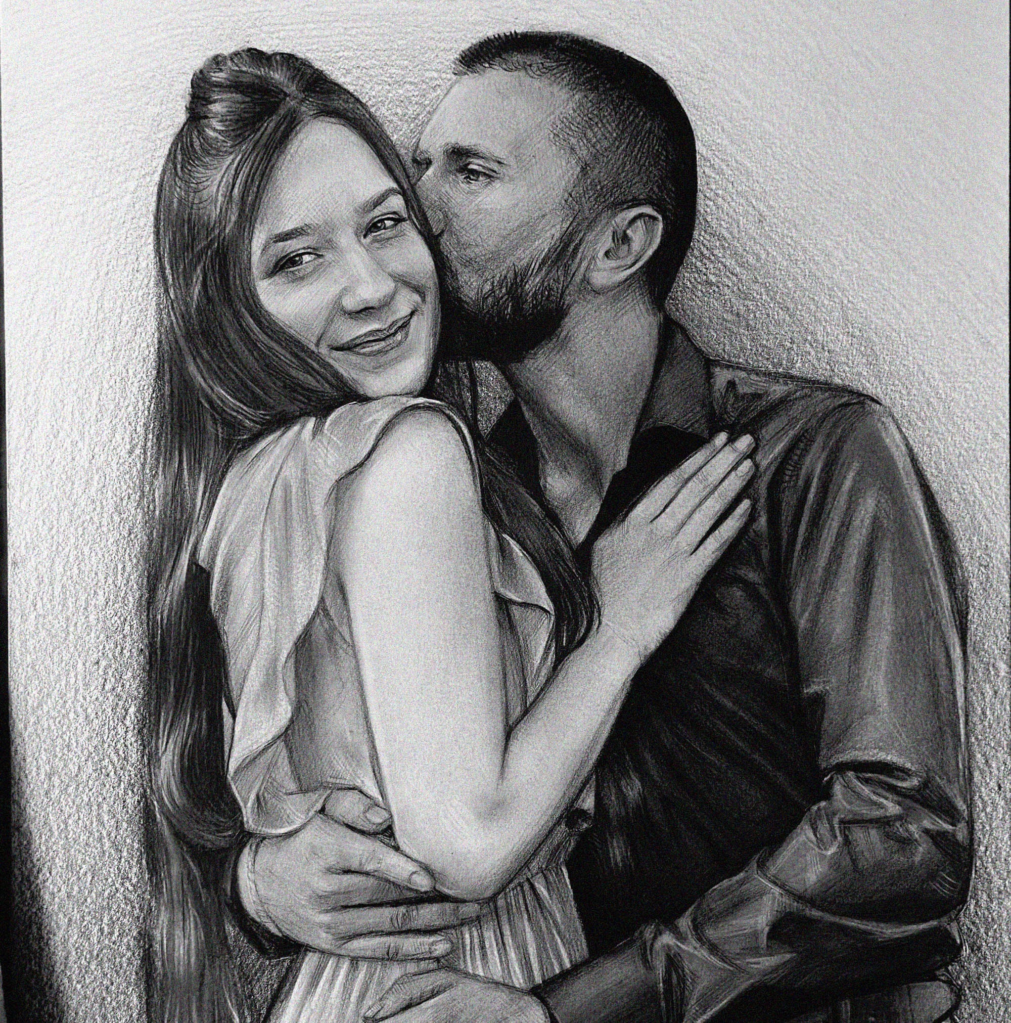 A detailed black and white graphite pencil drawing of a romantic couple embracing. A bearded man in a dark button-down shirt is gently kissing the cheek of a smiling woman. She has long hair tied half-up, is wearing a light-colored dress with ruffled sleeves, and rests her hand on his chest while his arms wrap around her waist.