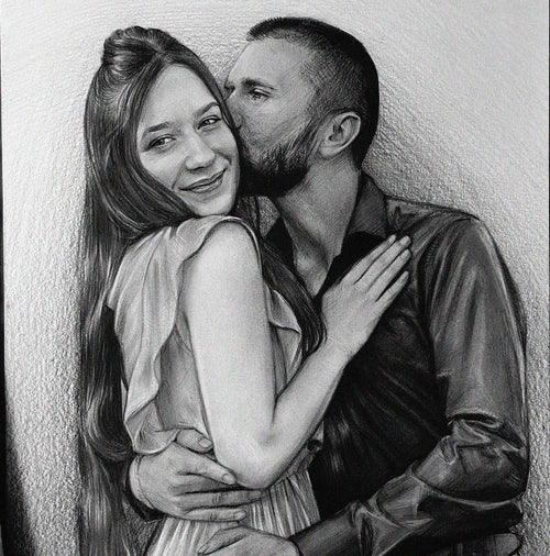 A detailed black and white graphite pencil drawing of a romantic couple embracing. A bearded man in a dark button-down shirt is gently kissing the cheek of a smiling woman. She has long hair tied half-up, is wearing a light-colored dress with ruffled sleeves, and rests her hand on his chest while his arms wrap around her waist.